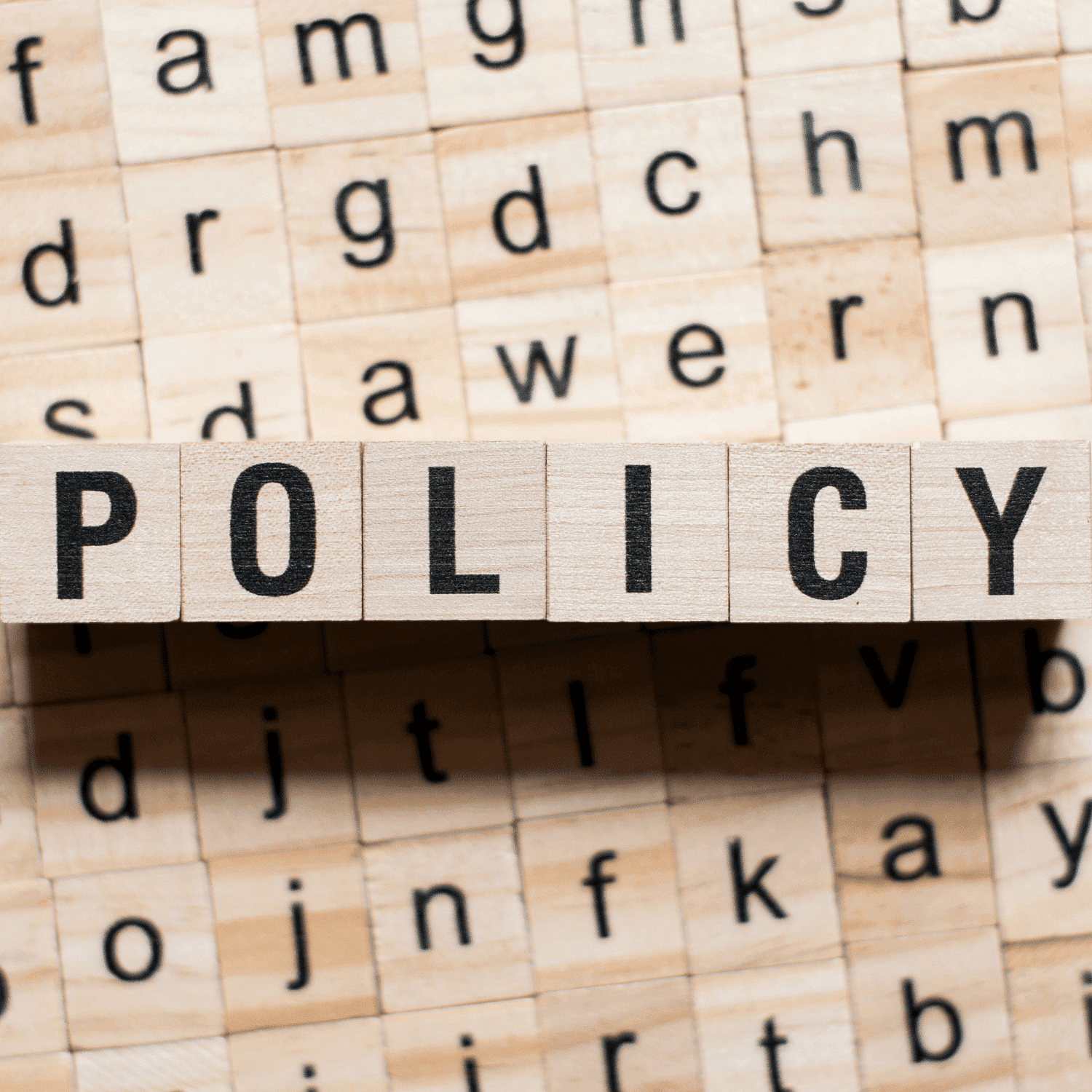 Scrabble tiles spelling "POLICY" on a board with random letters in the background.